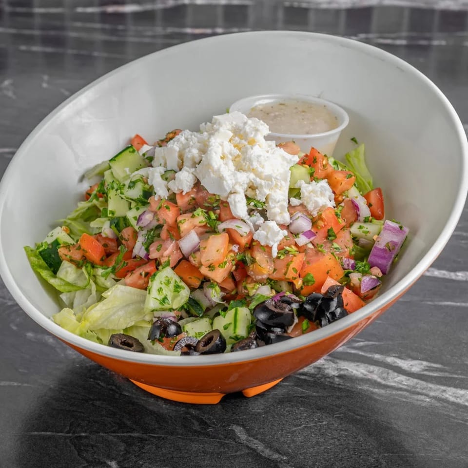 A vibrant salad with lettuce, tomatoes, cucumbers, olives, red onion, and feta cheese in a white and orange bowl.