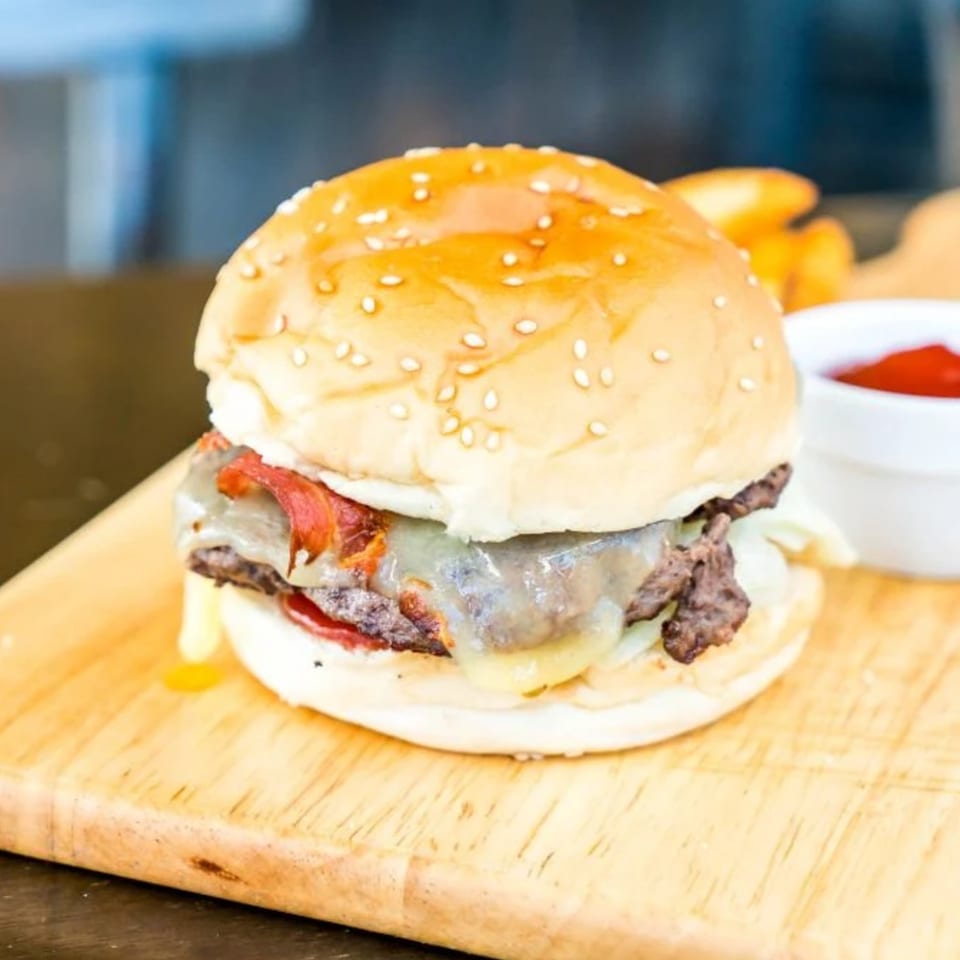 A juicy cheeseburger with bacon and melted cheese on a sesame seed bun, served with ketchup.